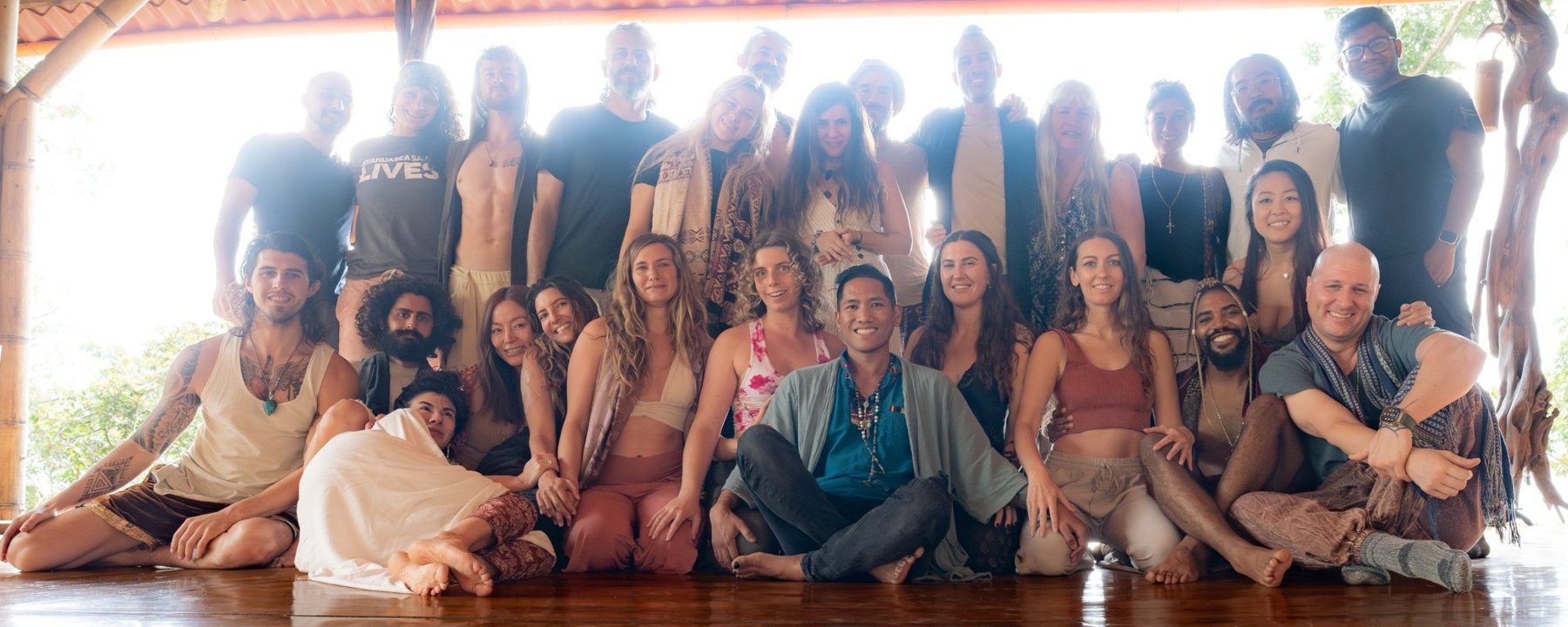 Ryan seated at the front of a group of smiling retreat participants under a bamboo pavilion