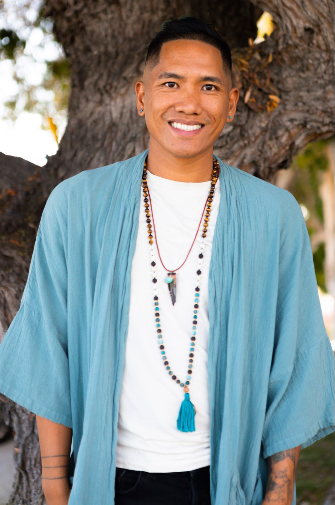 Ryan Foronda smiling in a teal robe in front of a large tree